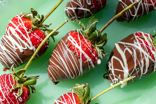 strawberries with stems dipped in chocolate and drizzled in white chocolate on green glass flat lay