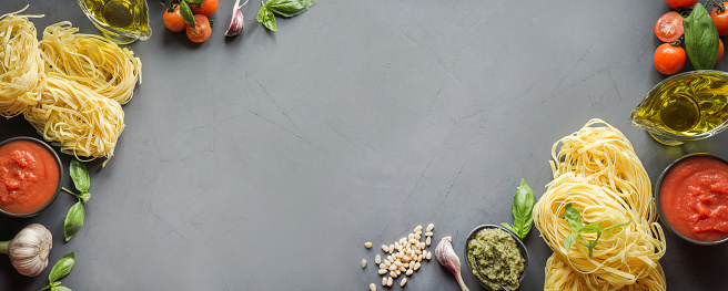 Banner with pasta ingredients for cooking Italian dishes - tagliatelle, tomatoes,pesto, basil, olive oil and garlic. Food pattern. Top view with space for text. Banner. Grey concrete background.