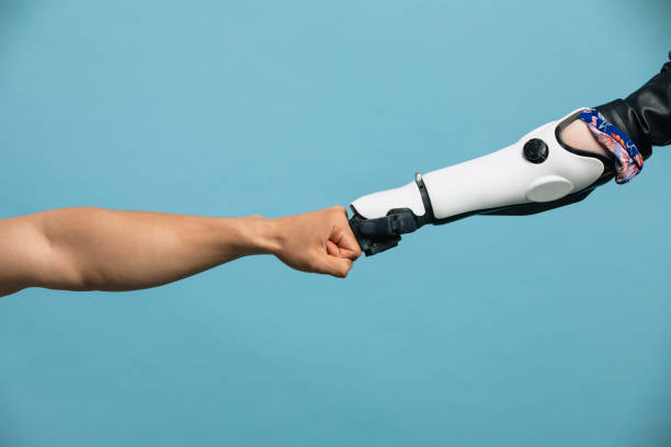 A Human and Robotic Arm Making a Fist Bump A human hand and a robotic hand, meeting in the middle, touching knuckles. robotic arm stock pictures, royalty-free photos & images