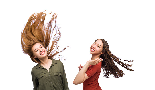 Mid body view of two pretty young woman flipping their hair over and looking at the camera smiling isolated on a white background.