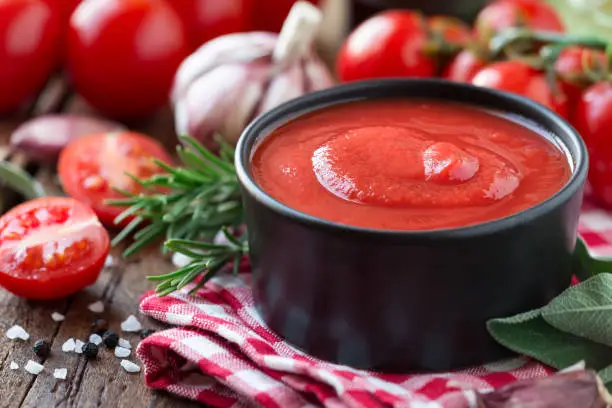Tomato sauce or ketchup in a black bowl with cooking ingredients at the background