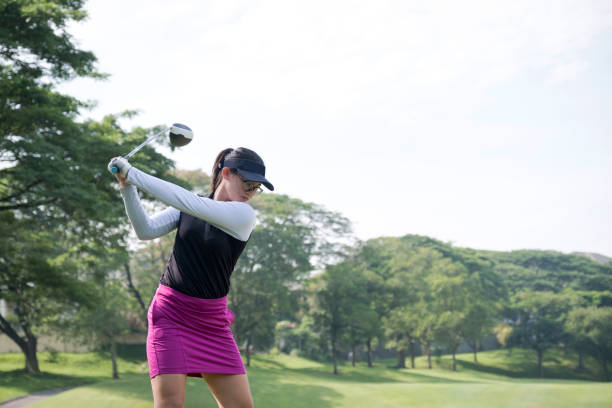 Determined golfer practices her golf swing Confident teenage golfer taking a shot on golf course. Female practicing on green landscape against clear sky. She is in sportswear during summer weekend. teenagers only golf teenager golf swing stock pictures, royalty-free photos & images