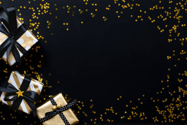 coffrets cadeaux dans divers papiers d’emballage de modèle d’or sur des paillettes dorées en forme d’étoile sur un fond noir. - confetti gold black star shape photos et images de collection