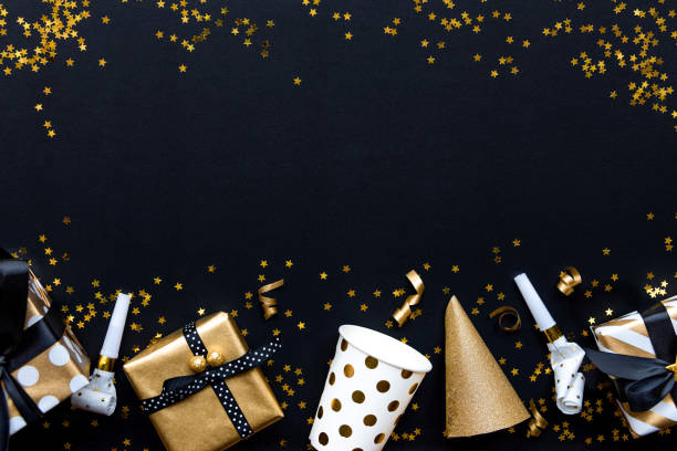 istock Gift boxes in various gold pattern wrapping papers and party accessories over star shaped golden sequins on a black background. 1149087767