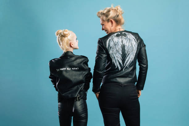 Fierce Females Two female friends are standing side-by-side in front of a blue background in a studio. They're both wearing leather jackets and looking happy. 12 13 years pre adolescent child female blond hair stock pictures, royalty-free photos & images