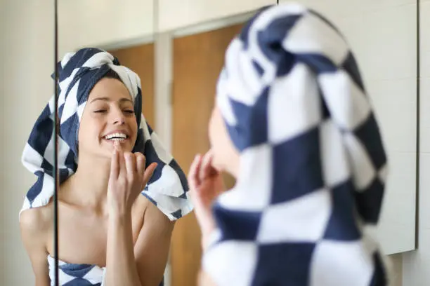 Young beautiful woman putting makeup on in the bathroom with a towel on the head