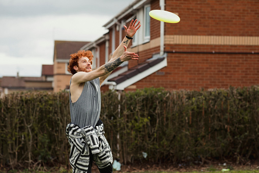 A side-view shot of a redhead caucasian man playing ultimate frisbee on a field, he is wearing casual clothing.