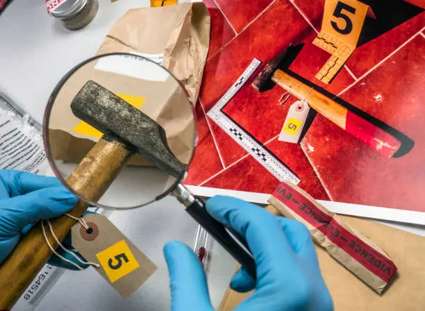 Photo of Expert police examines with magnifying glass a hammer in laboratory forensic equipment, conceptual image