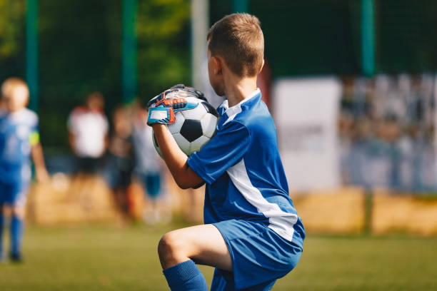 młody bramkarz piłki nożnej bramkarz łapanie piłki. młody chłopak bramkarz piłki nożnej. mecz piłki nożnej w słoneczny letni dzień. zajęcia sportowe dla dzieci. mecz piłki nożnej w tle. tapeta sportowa dla młodzieży - playing field kids soccer goalie soccer player zdjęcia i obrazy z banku zdjęć