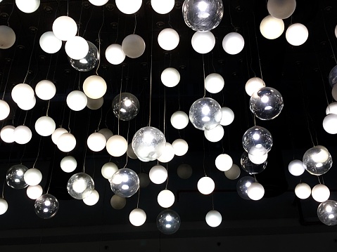 Lit opaque and translucent glass sphere lantern lights hanging displayed from a ceiling.