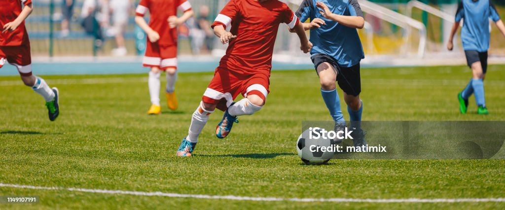 Fussball Soccer Spieler laufen mit Ball Fußballer Kicking Football Match. Junge Fußball-Spieler laufen nach dem Ball Kinder in den Fußball-Rot-und Blauen Uniformen. Fußballstadion im Hintergrund - Lizenzfrei Fußball Stock-Foto