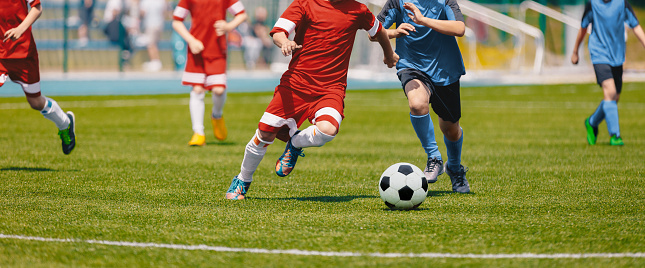 Futbolistas de fútbol corriendo con balón. Futbolistas que patean partido de fútbol. Jóvenes jugadores de fútbol corriendo después de la pelota. Niños en fútbol rojo y uniformes azules. Estadio de fútbol en el fondo photo