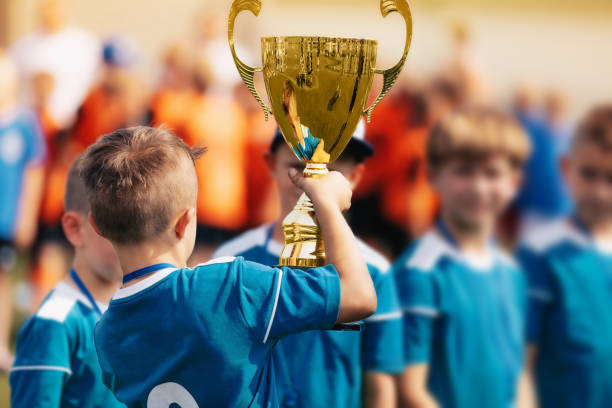 boy sosteniendo trofeo de oro y celebrando el éxito deportivo con el equipo - campeonato deportivo juvenil fotografías e imágenes de stock