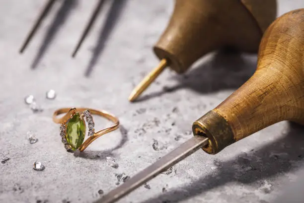 Gold ring with precious stones on the table, surrounded by jewelry repair tools, close-up