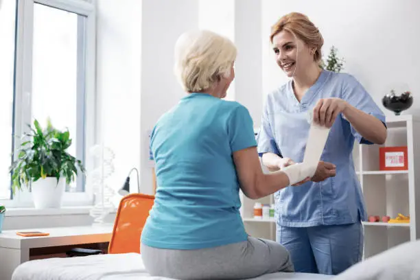 Medical care worker. Nice friendly female nurse smiling to her patient while doing her job in the hospital