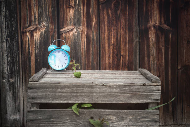Vintage image of a blue alarm clock displayed on an aged wooden crate, outside, with a weathered wooden wall as a background.