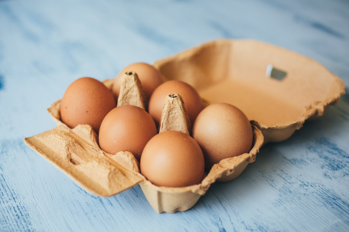 Eggs background. Closeup view of chicken eggs in carton box on wooden background. Food and health concept.