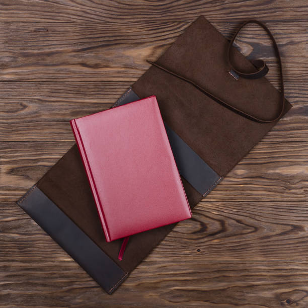 istock Brown opened handmade leather notebook cover with red notebook inside on wooden background. Stock photo of luxury business accessories. 1149125769