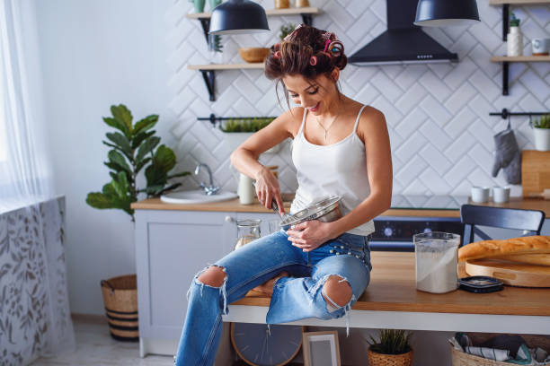 a mulher de sorriso bonita na roupa ocasional amassa uma massa de pão em uma placa de metal na cozinha à moda. cozimento bonito novo da mulher na cozinha home brilhante. - baking cake making women - fotografias e filmes do acervo