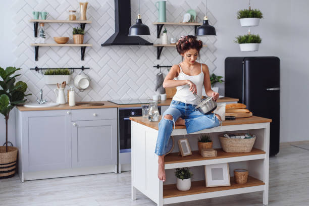 a mulher de sorriso bonita na roupa ocasional amassa uma massa de pão em uma placa de metal na cozinha à moda. cozimento bonito novo da mulher na cozinha home brilhante. - baking cake making women - fotografias e filmes do acervo