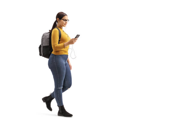 estudante fêmea que anda e que escolhe uma canção de seu telefone móvel - full length audio - fotografias e filmes do acervo