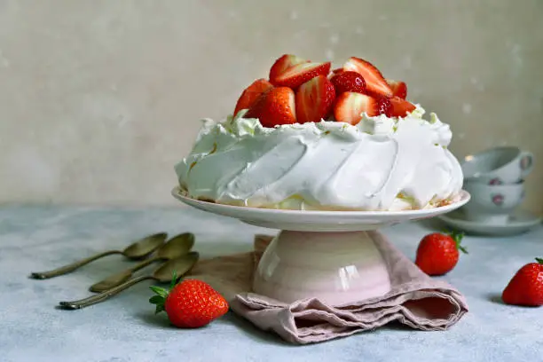 Delicious summer cake "Pavlova" with whipped cream and fresh strawberry on a light slate, stone or concrete background.