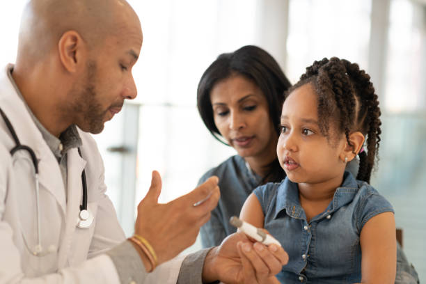 African American woman attends doctor's appointment with young daughter An African American mother is holding her young daughter on her lap. The child is having an appointment at a medical clinic. They are seated at a table across from the medical professional. The ethnic male doctor is teaching the mother and daughter about diabetes and how to use an insulin pen. injection-pen stock pictures, royalty-free photos & images