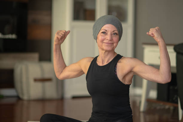 Senior woman with cancer flexing A senior woman with cancer flexes her muscles while sitting at home on her floor. She is smiling because she is getting stronger. food chain stock pictures, royalty-free photos & images