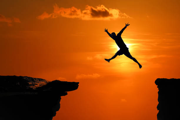 istock Silhouette of Men are jumped between high cliff at a red sky sunset 1149159122