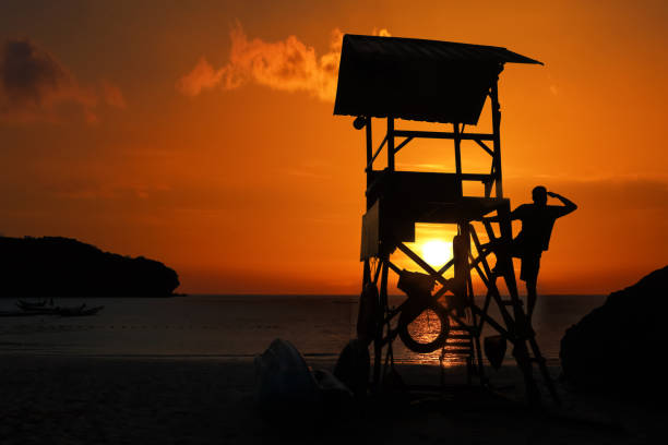 rettungsschwimmer bereit, sich um touristen an den stränden zu kümmern. asiatischer rettungsschwimmer steht bei sonnenaufgang auf dem turm - lifeguard orange nature beach stock-fotos und bilder