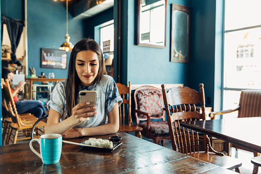 A Hispanic woman of the Millennial Generation is looking at her financial statement and showing a friend while eating lunch at a local sushi restaurant. She is using her bank's app to balance her monthly budget. Image taken in Utah, USA.