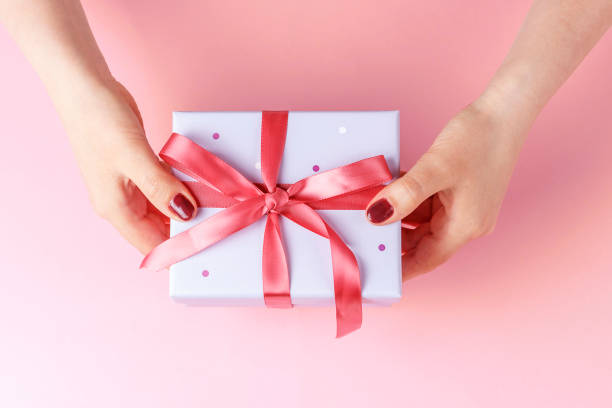 istock Female hands holding gift box with ribbon on pink background, top view 1149173845