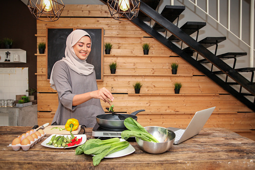 A young Malay Muslim female adult cooking in the kitchen and preparing food for Hari Raya Aidilfitri/ Eid-Ul-Fitr/ lunch, dinner, Ramadan.
