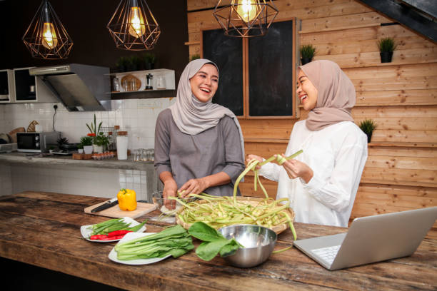 Young Malay Muslim female adults wearing hijab in the kitchen while preparing and cooking, and weaving ketupat for Hari Raya Aidilfitri/ Eid-Ul-Fitr