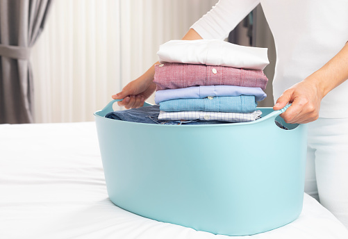 Women holding laundry basket and ironed shirts at home.