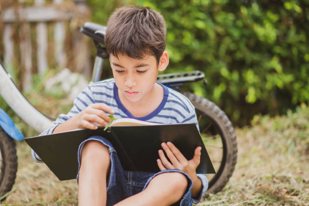 istock Little boy reading book sitting with bicycle in the park 1149186133