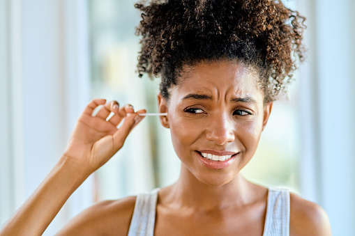 Shot of an attractive young woman cleaning her ears with a cotton bud during her morning routine at home