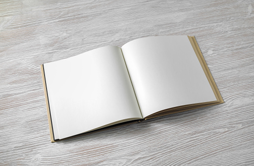 Opened blank square book on light wood table background.