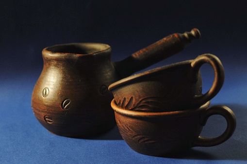 Clay coffee pot and two cups on blue background