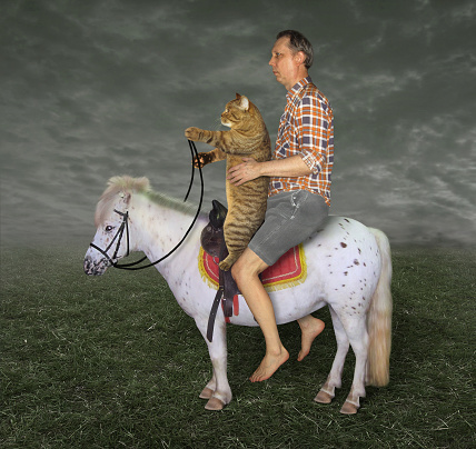 The barefoot man with his cat  is riding together on the white pony on the field.