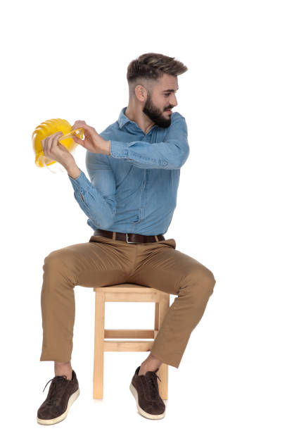 seated engineer student threatening with his yellow safety helmet - violence hat toughness blue imagens e fotografias de stock