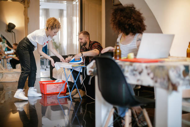 Young woman helping his flatmate iron a shirt Young woman looking at her friend helping their flatmate iron a shirt flatmate stock pictures, royalty-free photos & images