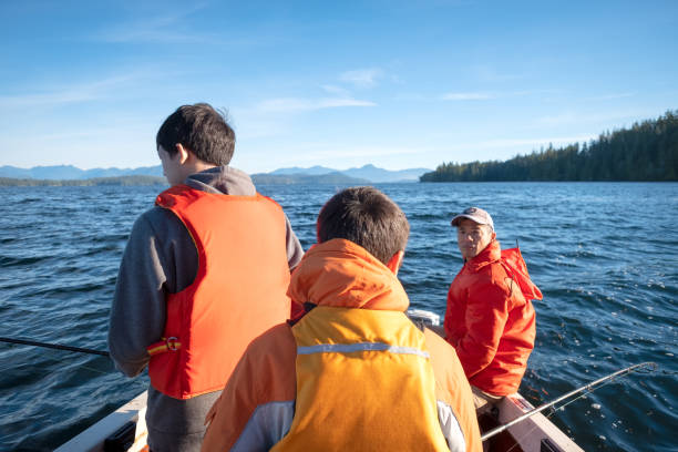 Asian Father and Multi-Ethnic Teen Brothers Fishing in Motor Boat Eurasian brothers ocean salmon fishing.   Bamfield, Vancouver Island, British Columbia, Canada family motorboat stock pictures, royalty-free photos & images