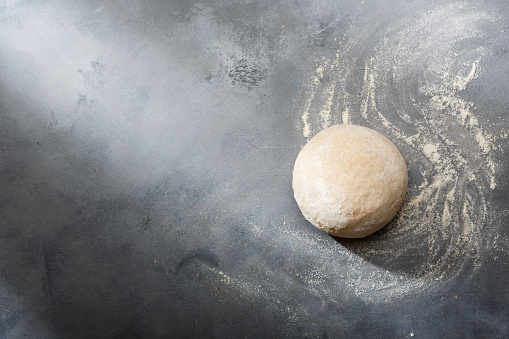 Risen or proved yeast dough for bread or pizza on a floured slate surface. Top view