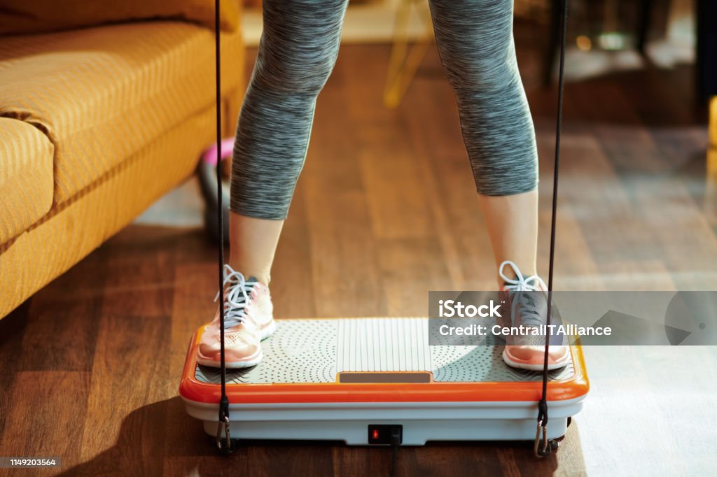 Closeup on sports woman training using vibration power plate Closeup on fit sports woman in fitness clothes at modern home training using vibration power plate. Shaking Stock Photo