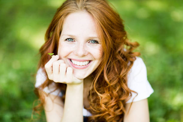beautiful positive young redhead woman with blue eyes in nature young beautiful woman with beautiful smile, red hair, blue eyes, freckles, lucky clover, jeans pants, leisure, holiday, relax, joyful, joy freckle photos stock pictures, royalty-free photos & images