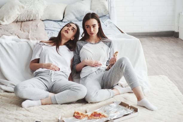 Overeating is never good. Twins have full stomach with pizza. Nice bedroom at daytime Overeating is never good. Twins have full stomach with pizza. Nice bedroom at daytime. never the same stock pictures, royalty-free photos & images