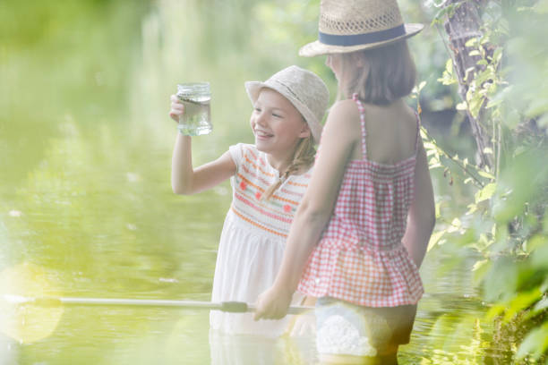 istock Smiling girls looking at jar while standing in lake 1149219983