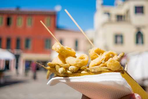 close up of hands holding street food consisting in fried fish inside a paper cone in venice during sunny summer day