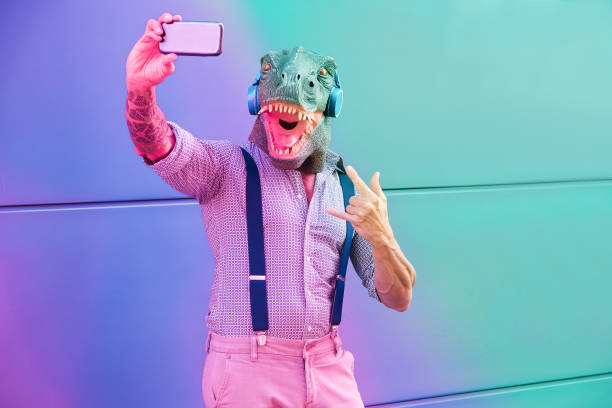 homme tatoué avec le masque de t-rex utilisant le smartphone tout en écoutant la musique-mâle aîné fou prenant le selfie avec l’application de téléphone mobile-montage de filtre violet et bleu radial-focus sur le visage - animal cell photos photos et images de collection
